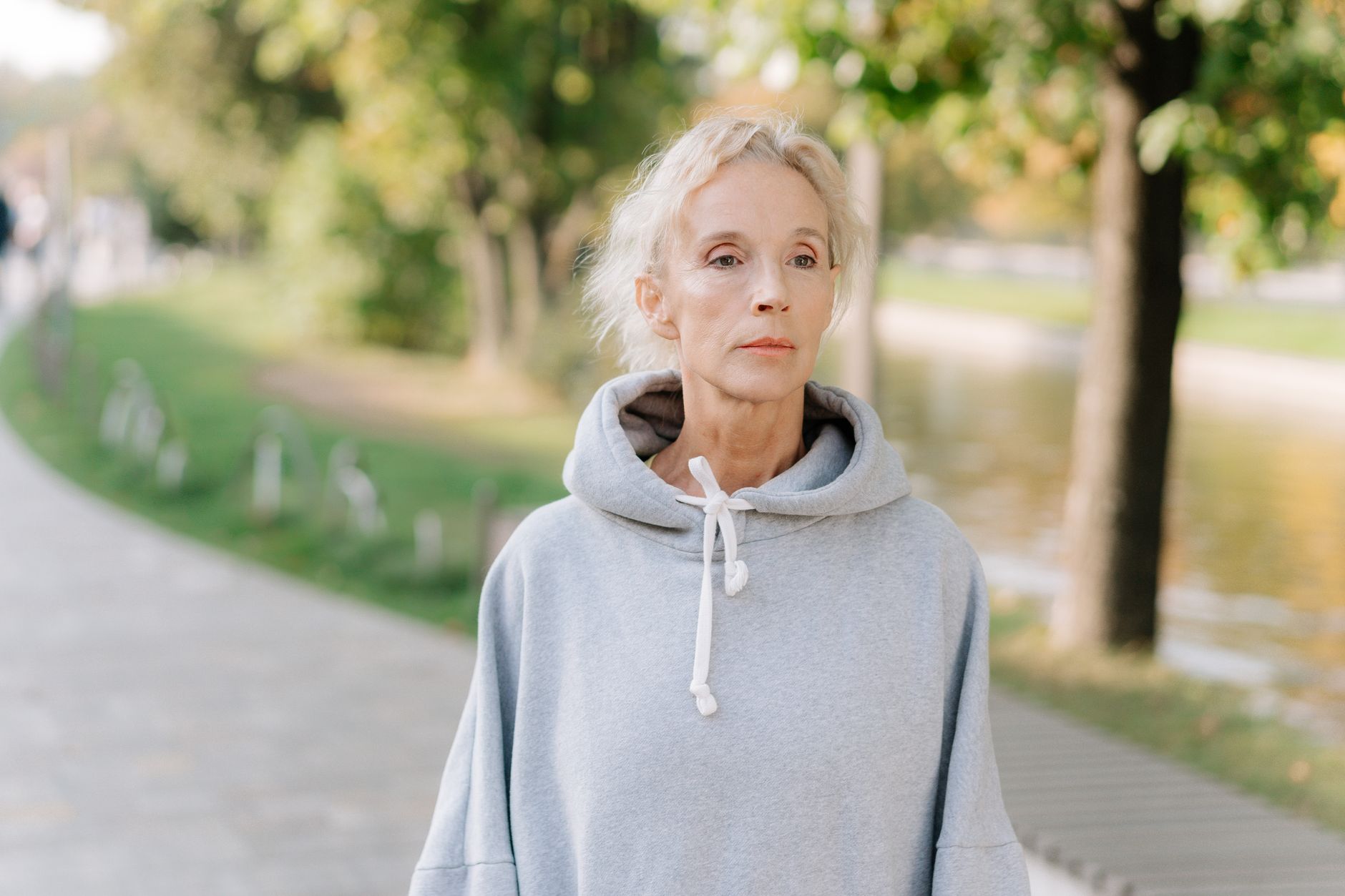 A woman in her fifties with short fair hair and a grey hoodie standing on a riverside path in a park